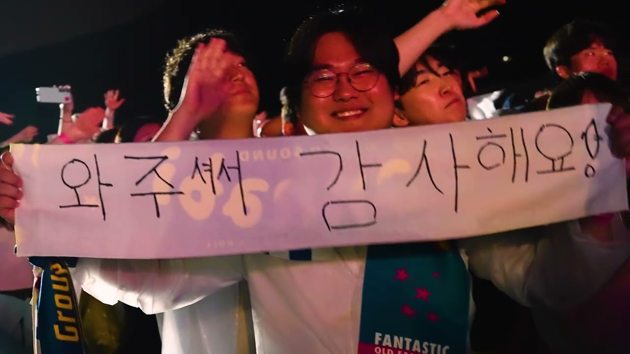 야간 행사장에서 관객들이 ‘와주셔서 감사해요!’ 현수막을 들고 웃는 장면