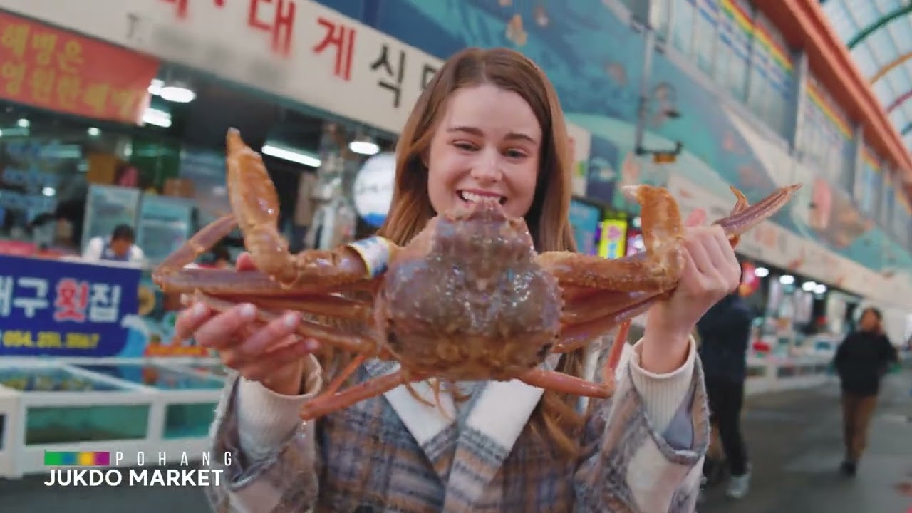 수산시장 안에서 여성이 큰 게를 양손으로 들어 보이는 장면